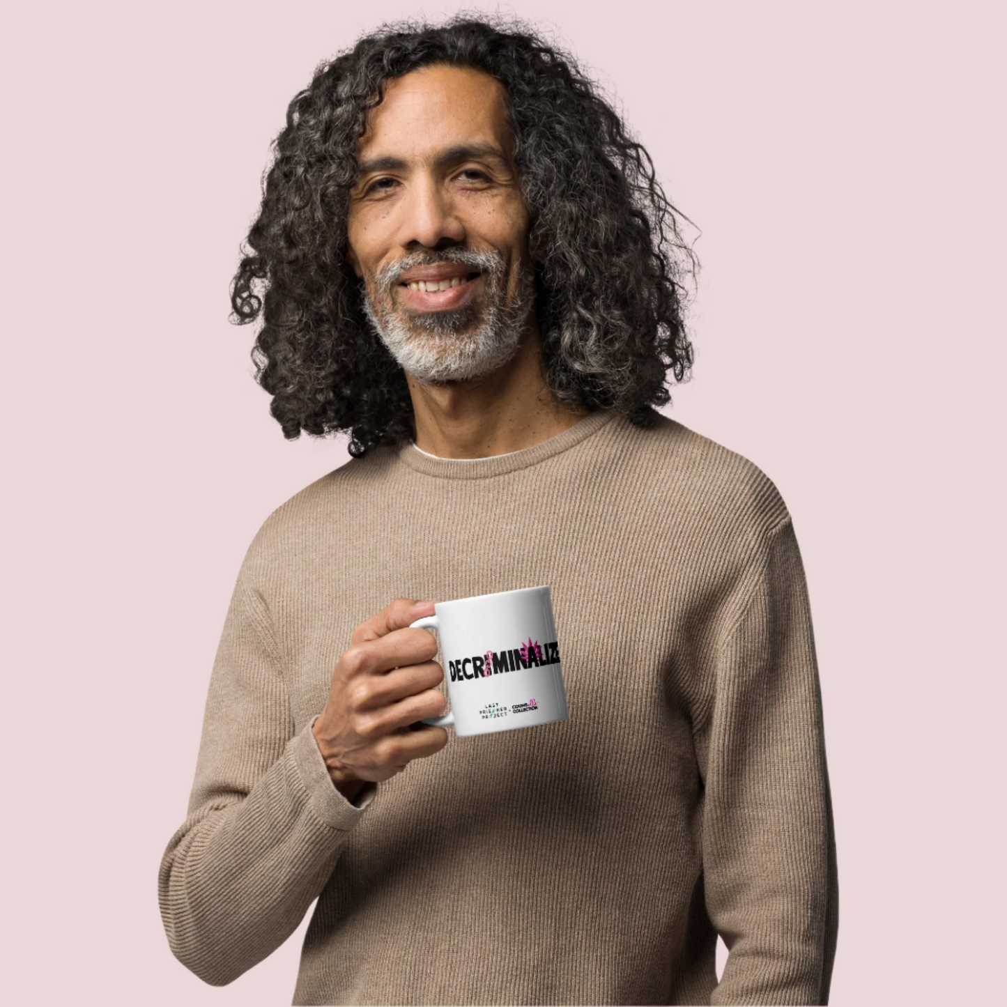A brown skinned man with curly hair wearing a beige long sleeved shirt holding a white mug with the text "decriminalize" on the front.
Last Prisoner Project and Counselle Collection® logos at the bottom of the mugs.