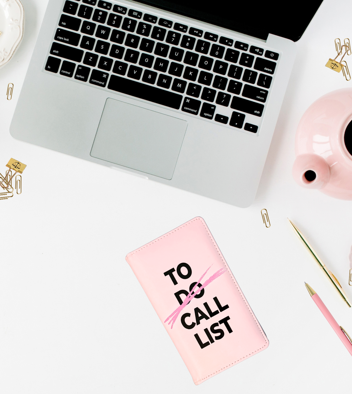 TO CALL LIST Business card holder book in blush pink,laying closed on white background, surrounded by a laptop, assorted pens and other stationery items.