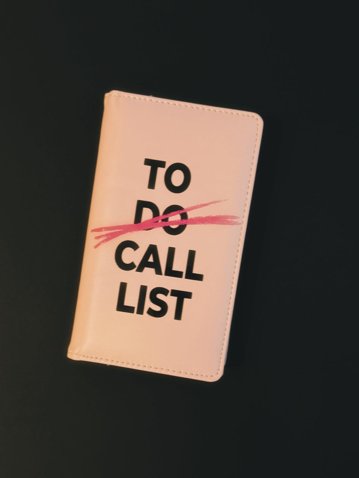 A blush pink, vegan leather business card holder with black text that says “to call list”
