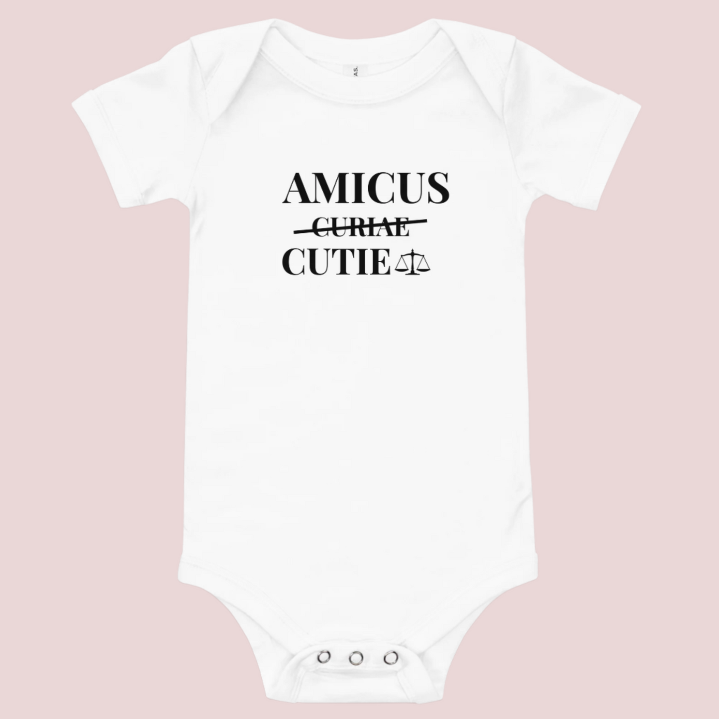 A white infant onesie featuring in black text, the words "AMICUS", "CUTIE", and a stricken out word "CURIAE", with an illustration of justice scales.