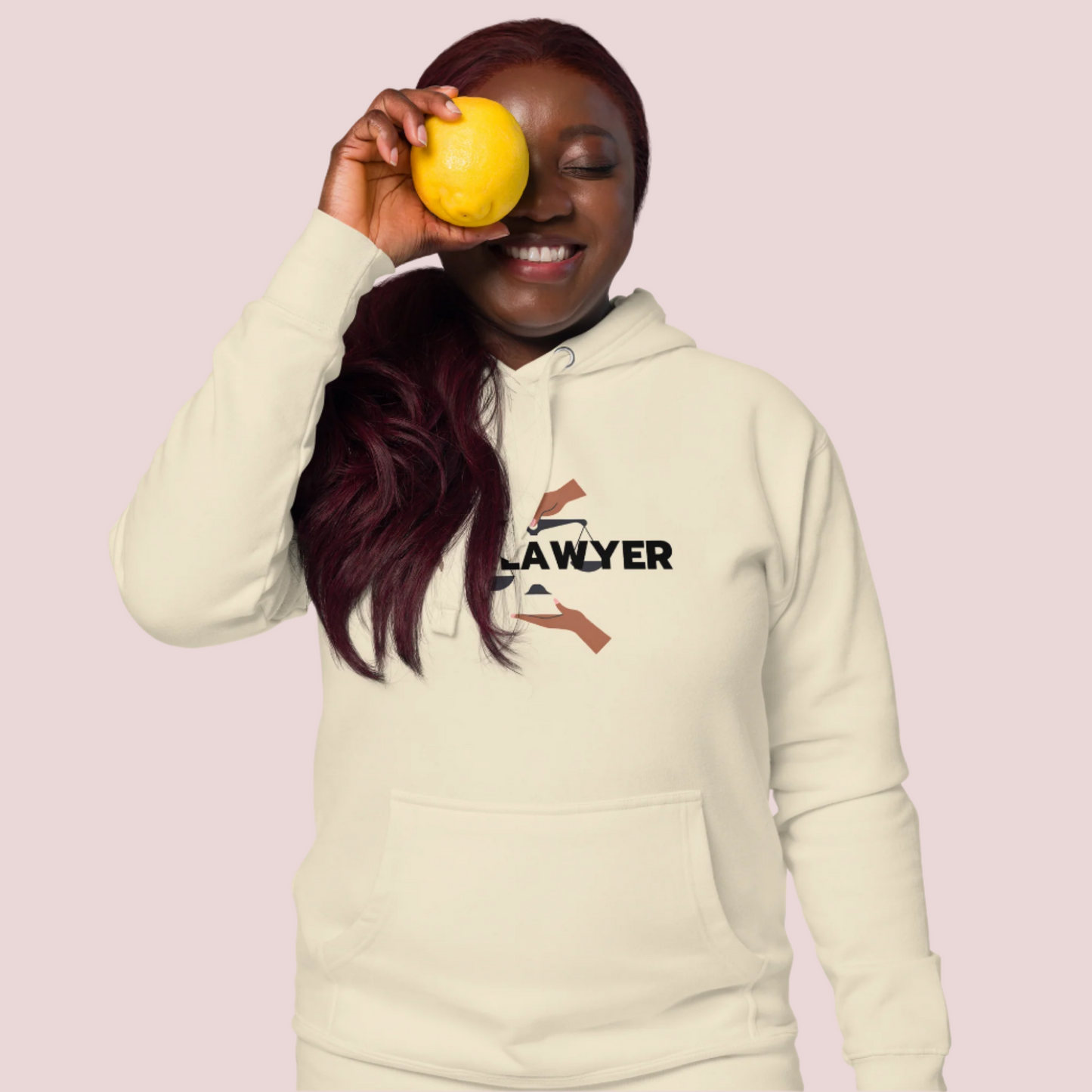 A model wearing a cream hoodie with the words "Black Lawyer" on it and a woman's hand holding an imbalanced justice scale.