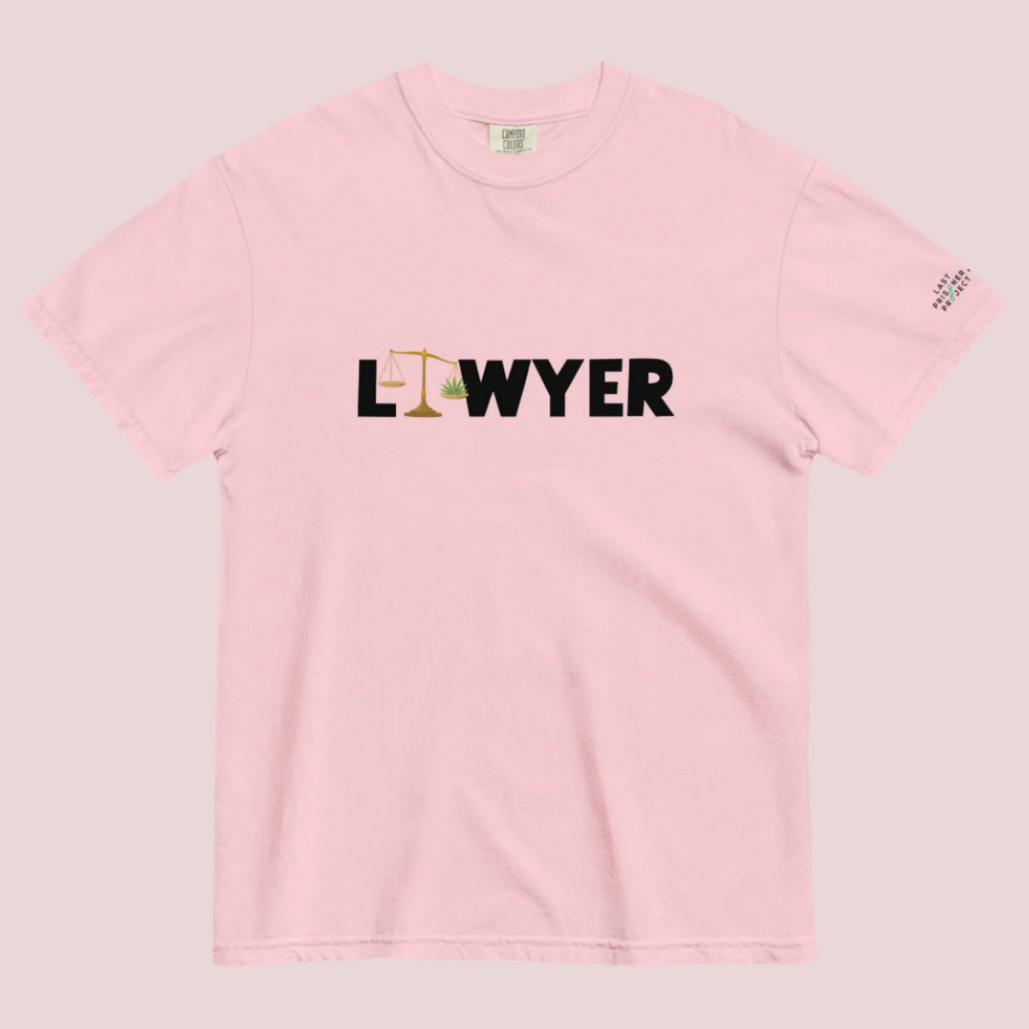 A pink crewneck tee showing the text "LAWYER", with the letter "A" stylized as a set of tilted justice scales, with one scale pan containing cannabis leaves while the other pan remains empty, with The last Prisoner Project x The Counselle Collection logo on the left sleeve.