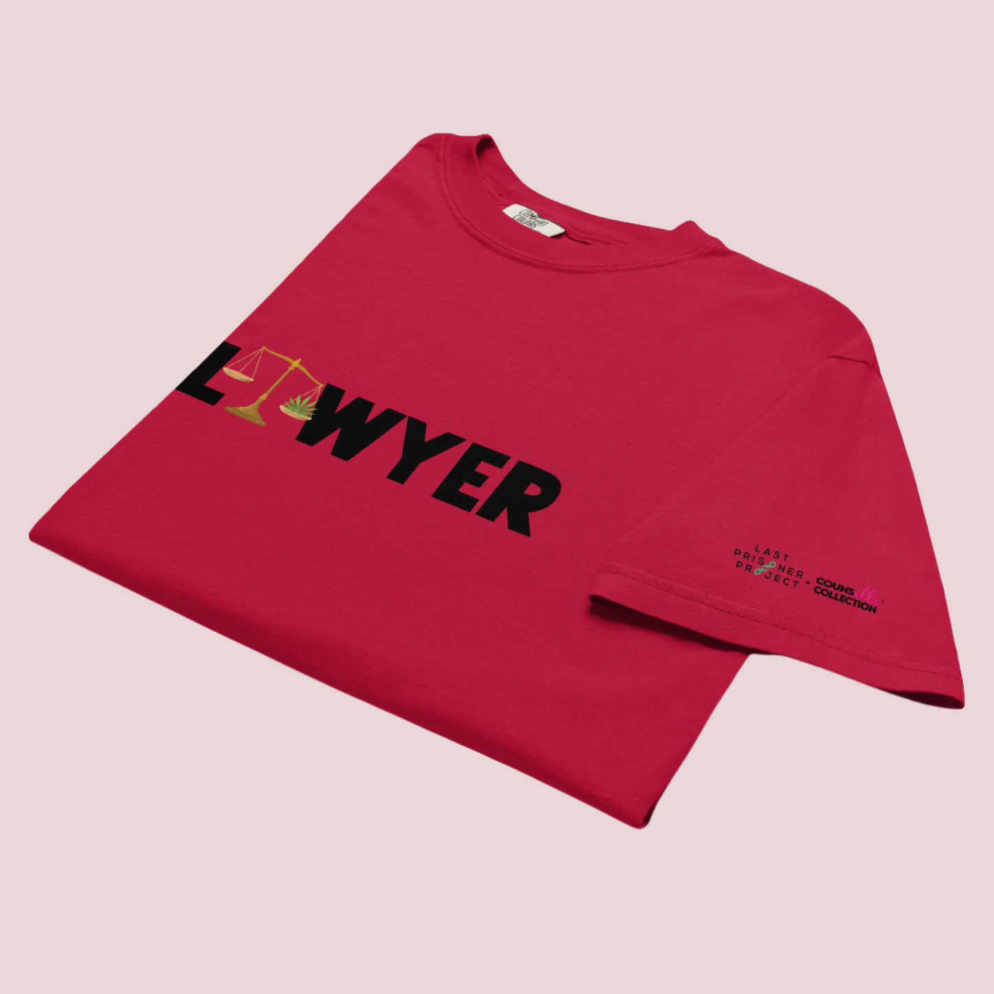 A red crewneck tee showing the text "LAWYER", with the letter "A" stylized as a set of tilted justice scales, with one scale pan containing cannabis leaves while the other pan remains empty, with The last Prisoner Project x The Counselle Collection logo on the left sleeve.