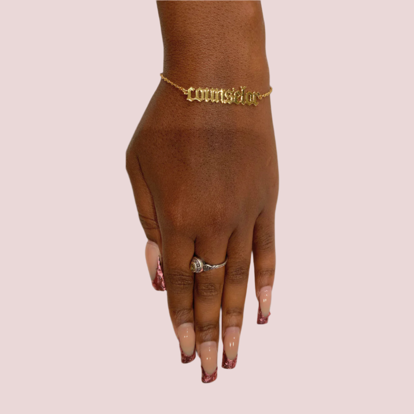 A gold chain bracelet featuring the word "counselor" in old English text worn on a person's left hand.