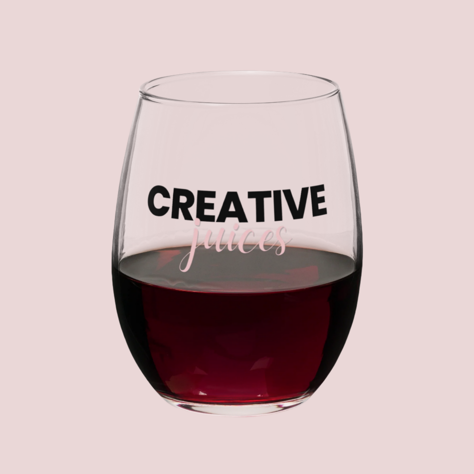 A stemless wine glass with the text "creative juices" on the front. Half filled with red wine.