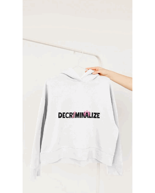 A white hoodie showing the text "DECRIMINALIZE", with a broken pink chain over the first letter "I" and pink cannabis leaves behind the letter "A".