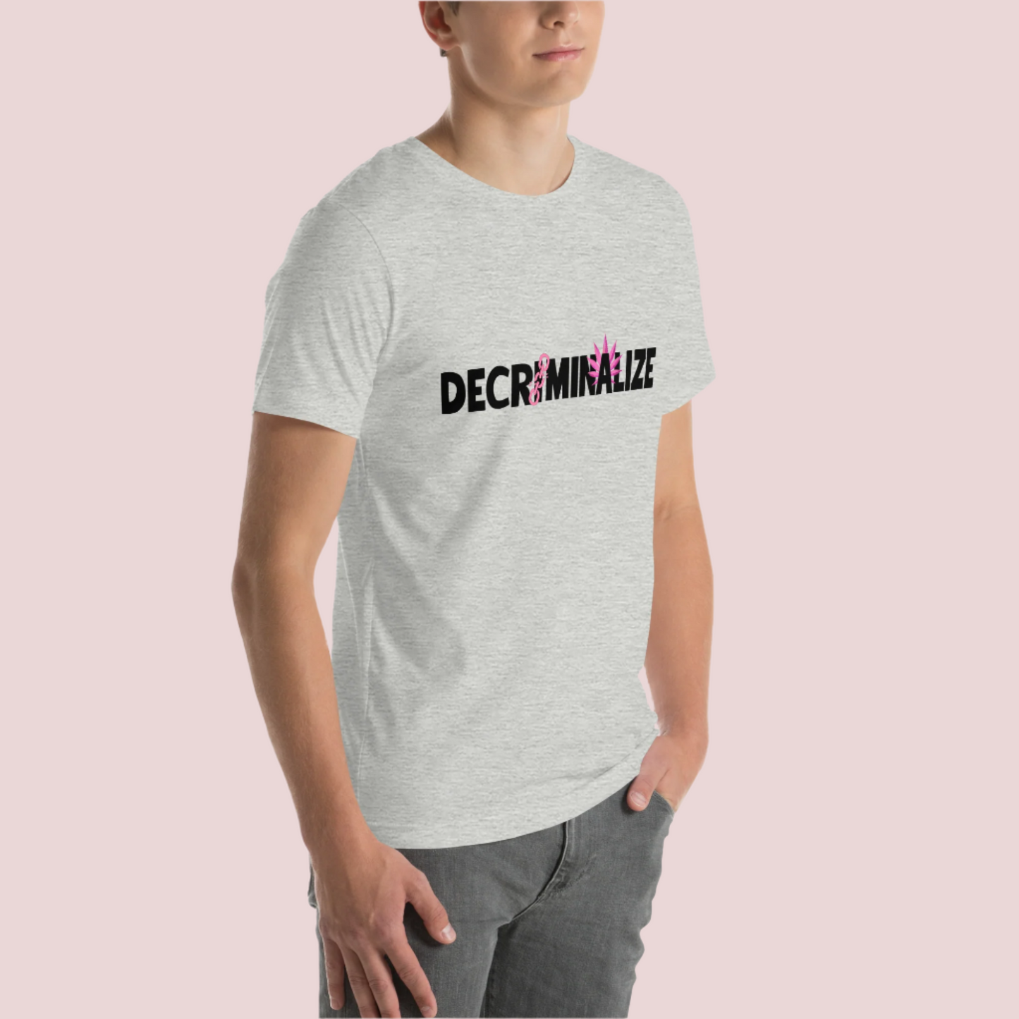 A person wearing a grey crewneck tee showing the text "DECRIMINALIZE", with a broken pink chain over the first letter "I" and pink cannabis leaves behind the letter "A" .