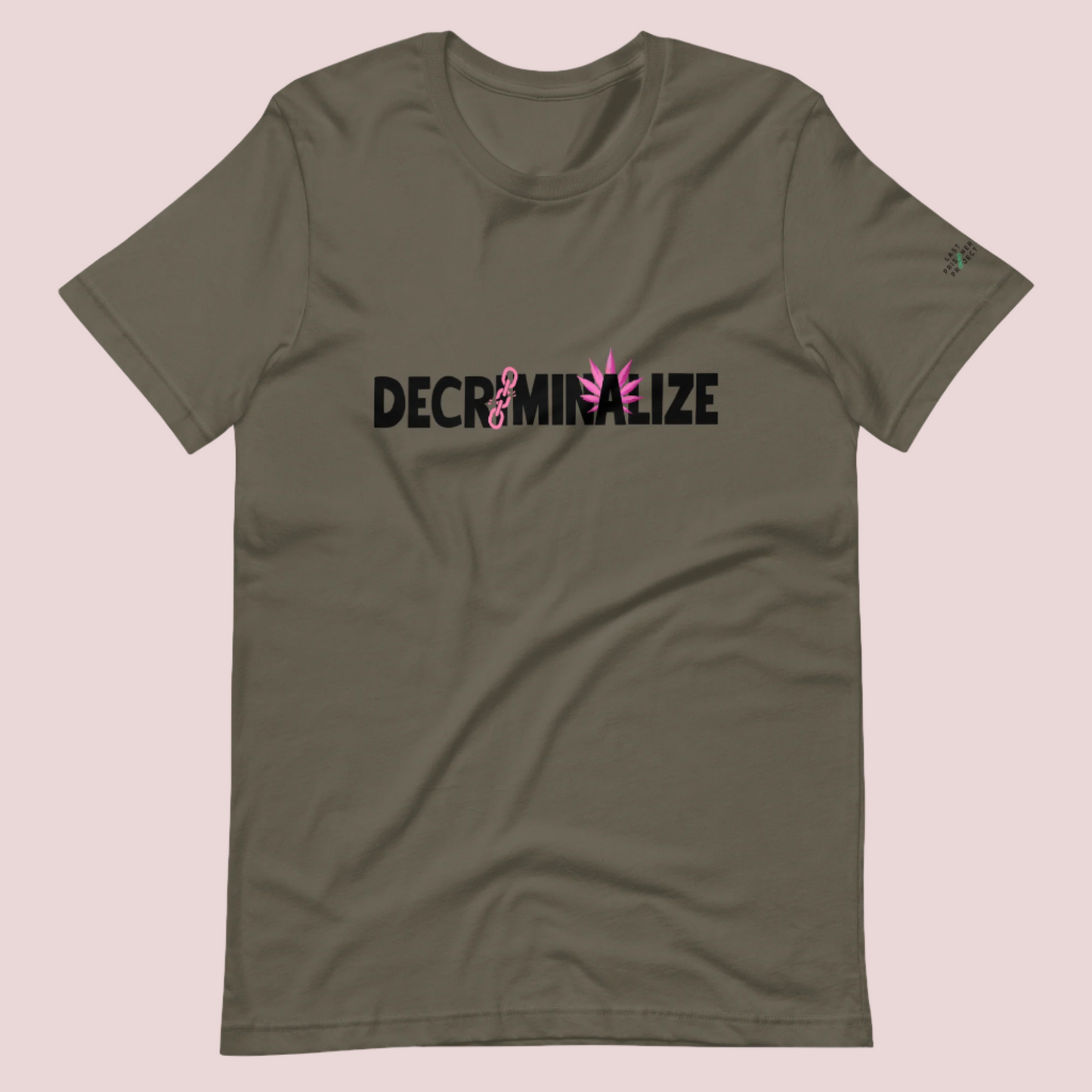 An army green crewneck tee showing the text "DECRIMINALIZE", with a broken pink chain over the first letter "I" and pink cannabis leaves behind the letter "A" . The Last Prisoner Project x The Counselle Collection logo on the left sleeve.