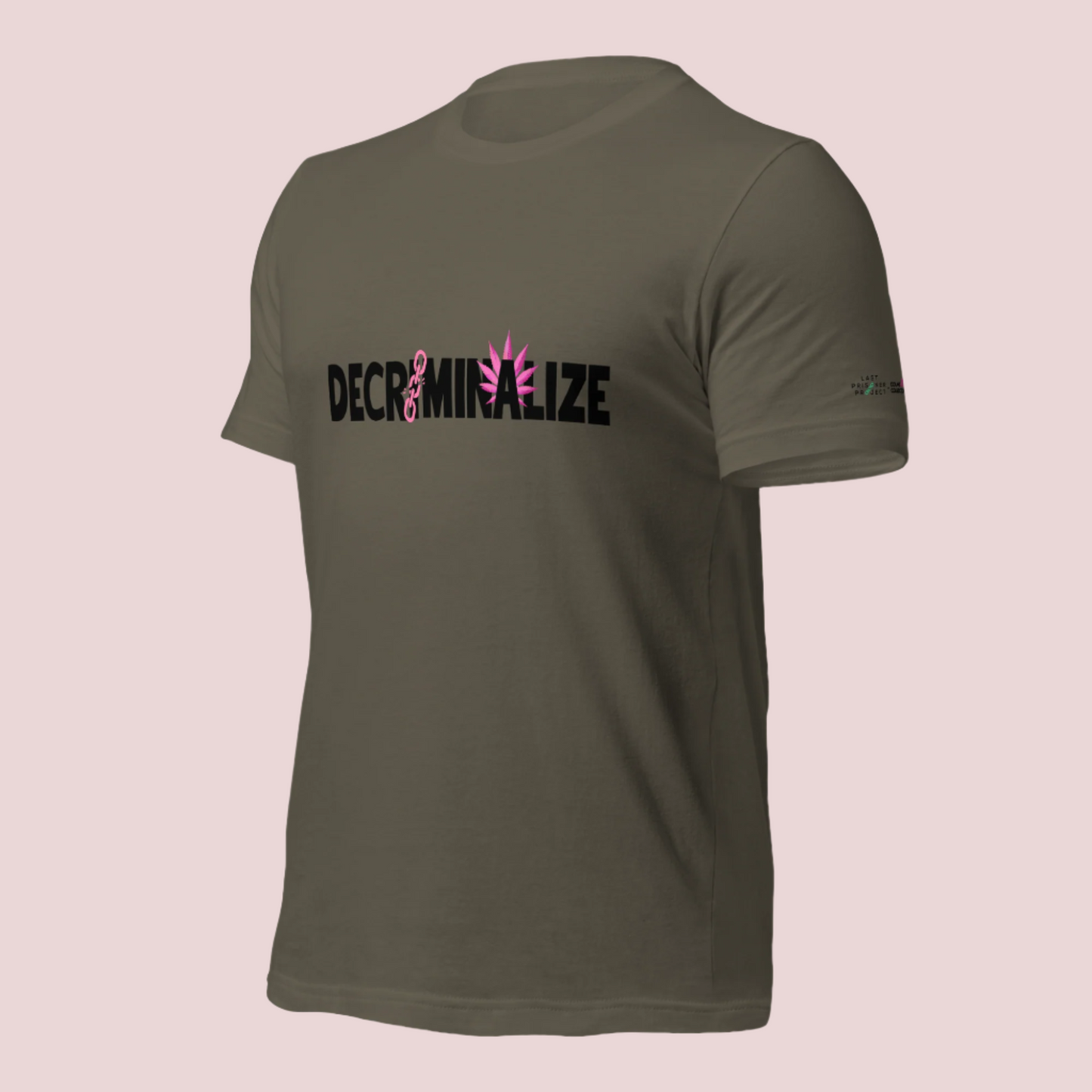 An army green crewneck tee showing the text "DECRIMINALIZE", with a broken pink chain over the first letter "I" and pink cannabis leaves behind the letter "A" . The Last Prisoner Project x The Counselle Collection logo on the left sleeve.
