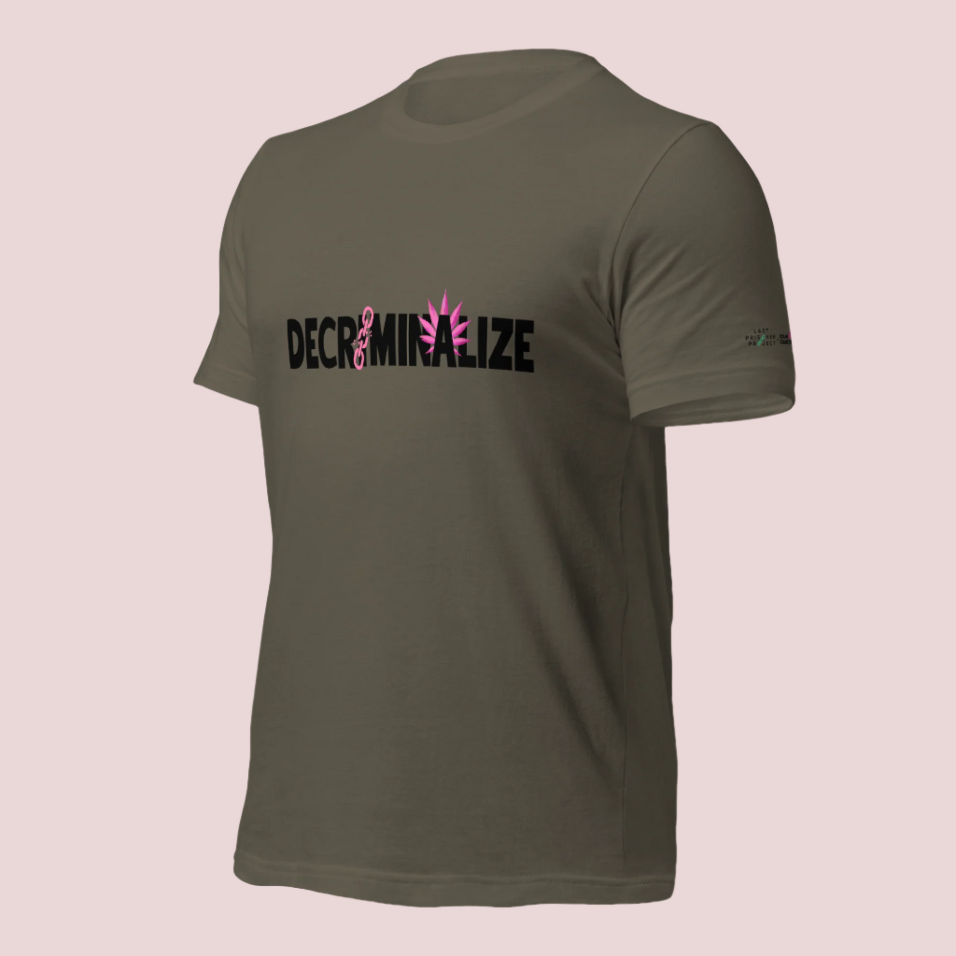 An army green crewneck tee showing the text "DECRIMINALIZE", with a broken pink chain over the first letter "I" and pink cannabis leaves behind the letter "A" . The Last Prisoner Project x The Counselle Collection logo on the left sleeve.