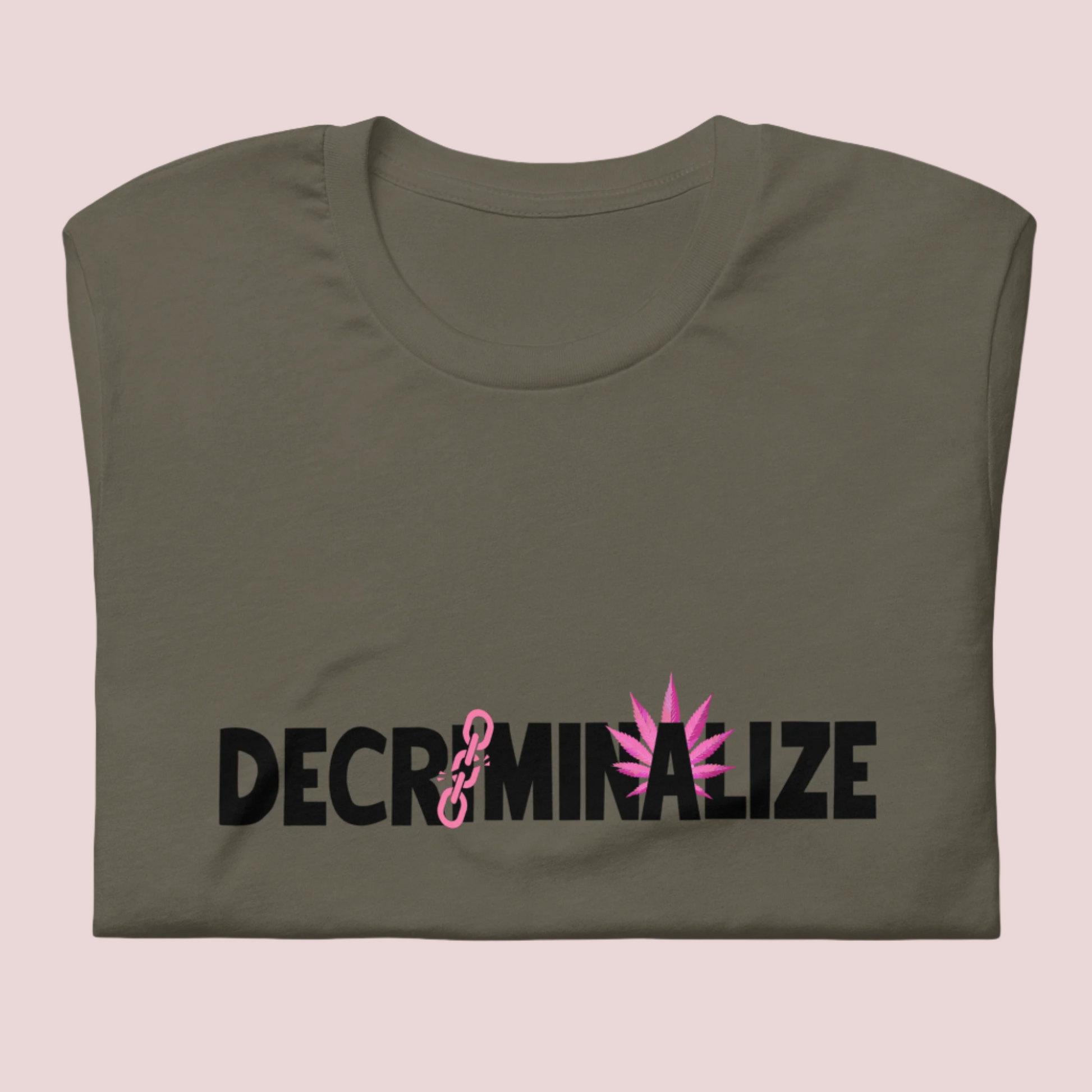 A folded army green crewneck tee showing the text "DECRIMINALIZE", with a broken pink chain over the first letter "I" and pink cannabis leaves behind the letter "A" .