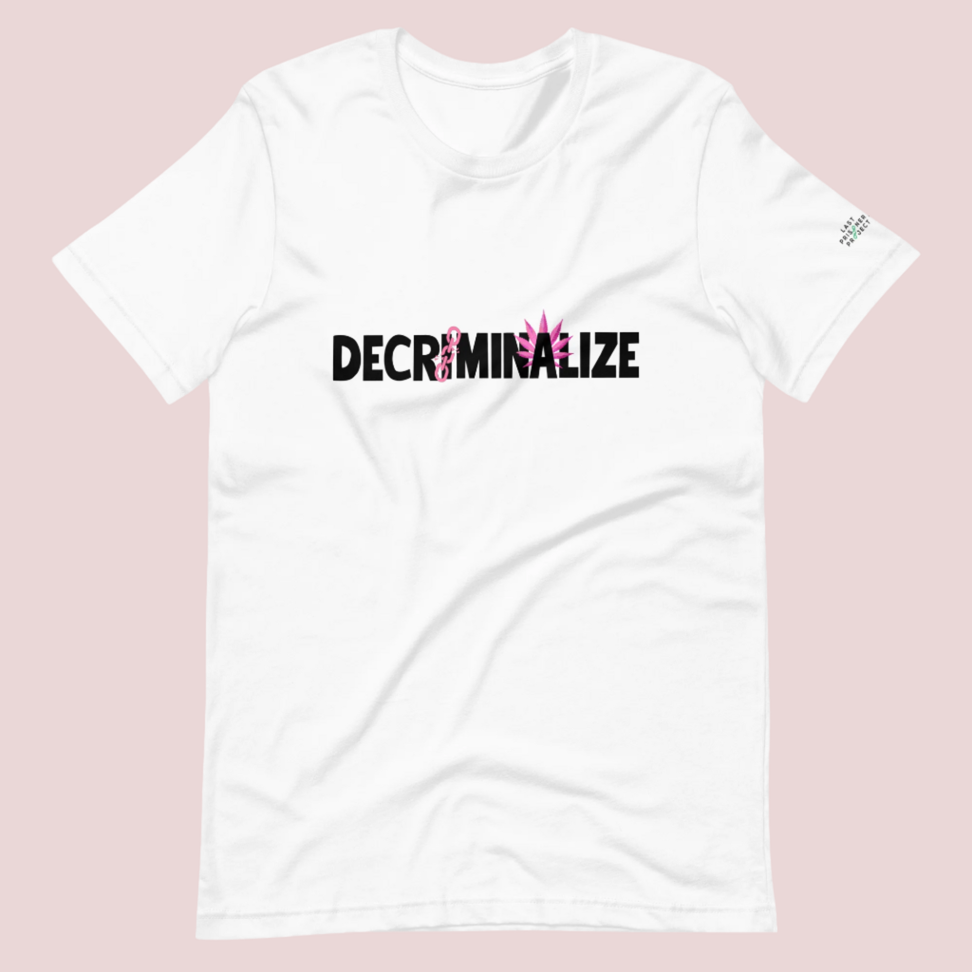 A white crewneck tee showing the text "DECRIMINALIZE", with a broken pink chain over the first letter "I" and pink cannabis leaves behind the letter "A". The Last Prisoner Project x The Counselle Collection logo on the left sleeve.