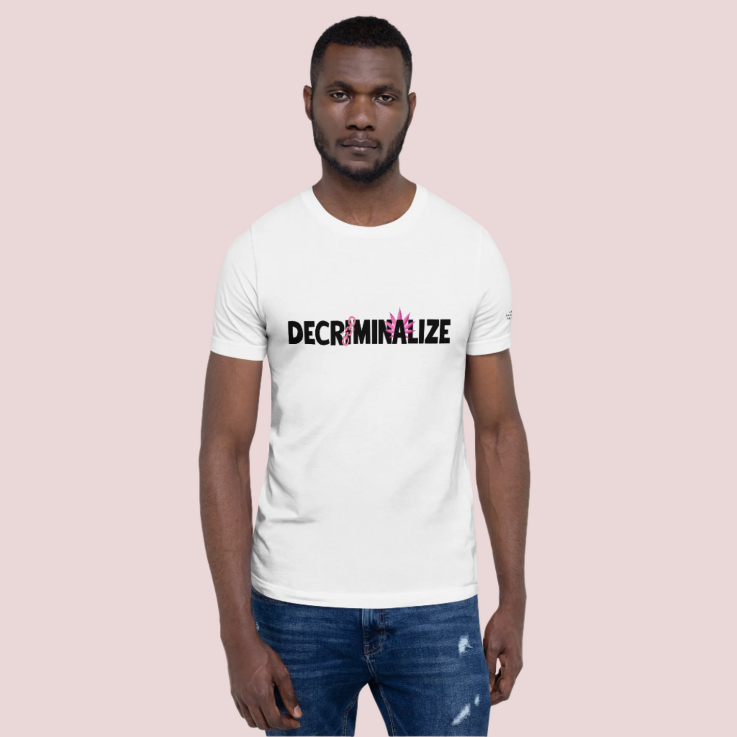 A person wearing a white crewneck tee showing the text "DECRIMINALIZE", with a broken pink chain over the first letter "I" and pink cannabis leaves behind the letter "A" . The Last Prisoner Project x The Counselle Collection logo on the left sleeve.
