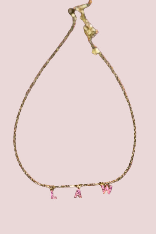 A gold necklace which features the letters "LAW" in block font, and embellished with pink stones.