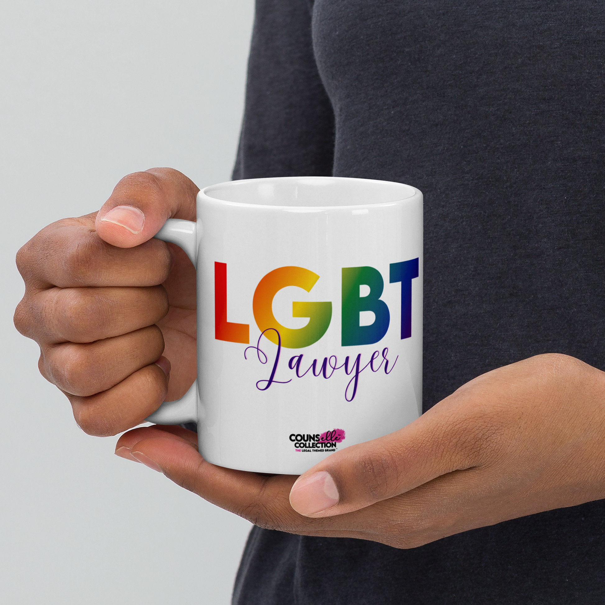 A model holding a white mug featuring the text "LGBT" in a rainbow-colored font, "Lawyer" in purple script, and the counsellecollection logo at the bottom  of the design.