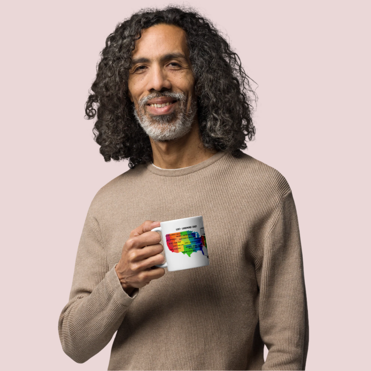 A person holding a white mug featuring a map of the USA in rainbow colors, with case titles of LGBT+ landmark cases written across in black text