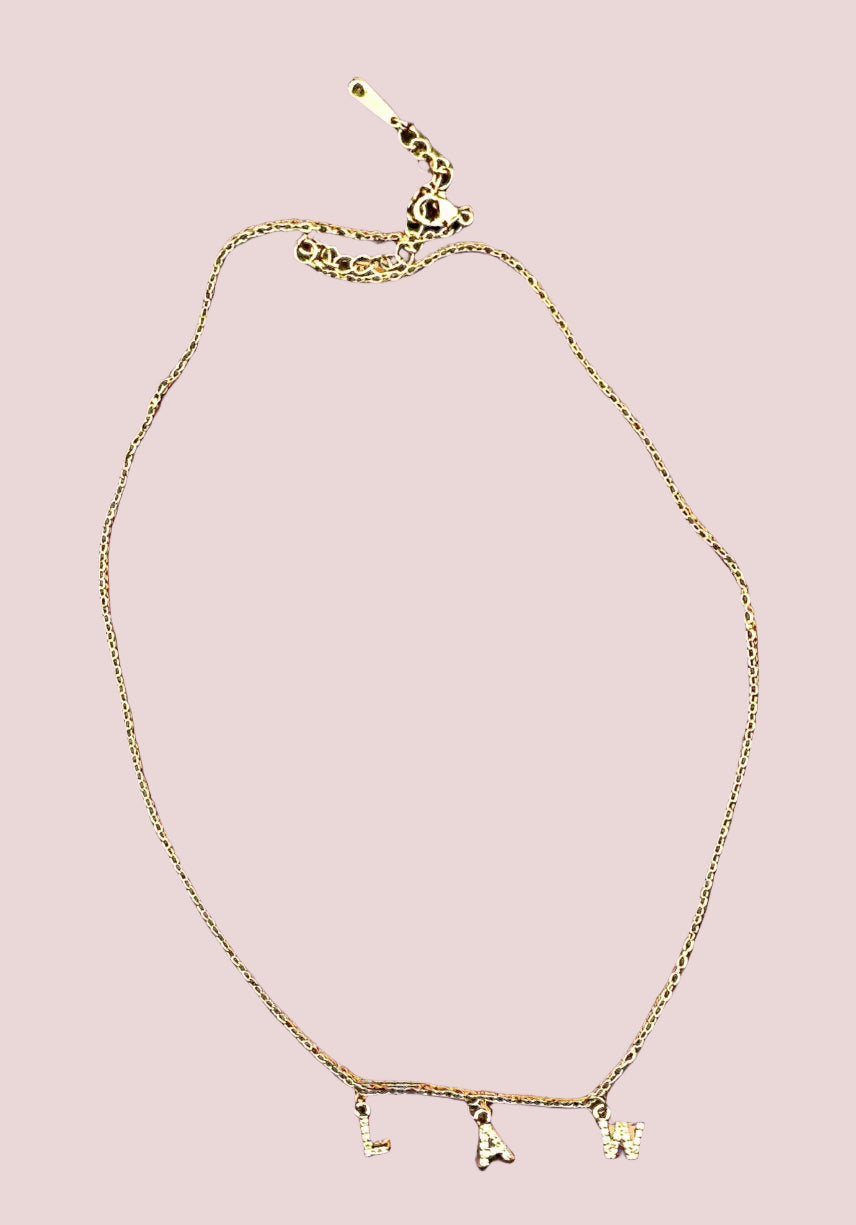 A gold necklace which features the letters "LAW" in block font, and embellished with white stones.