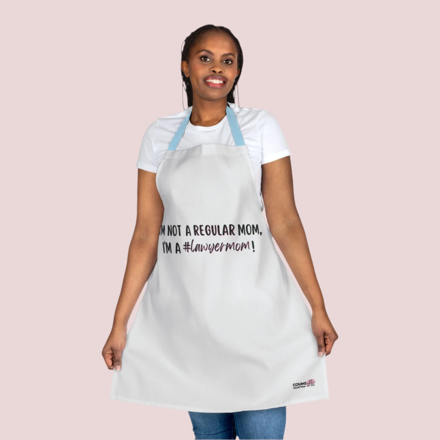 A white apron with the text "I'm not a regular mom, I'm a #lawyermom!" and the counsellecollection logo on the bottom right corner. The apron has a blue neck strap and blue belt.