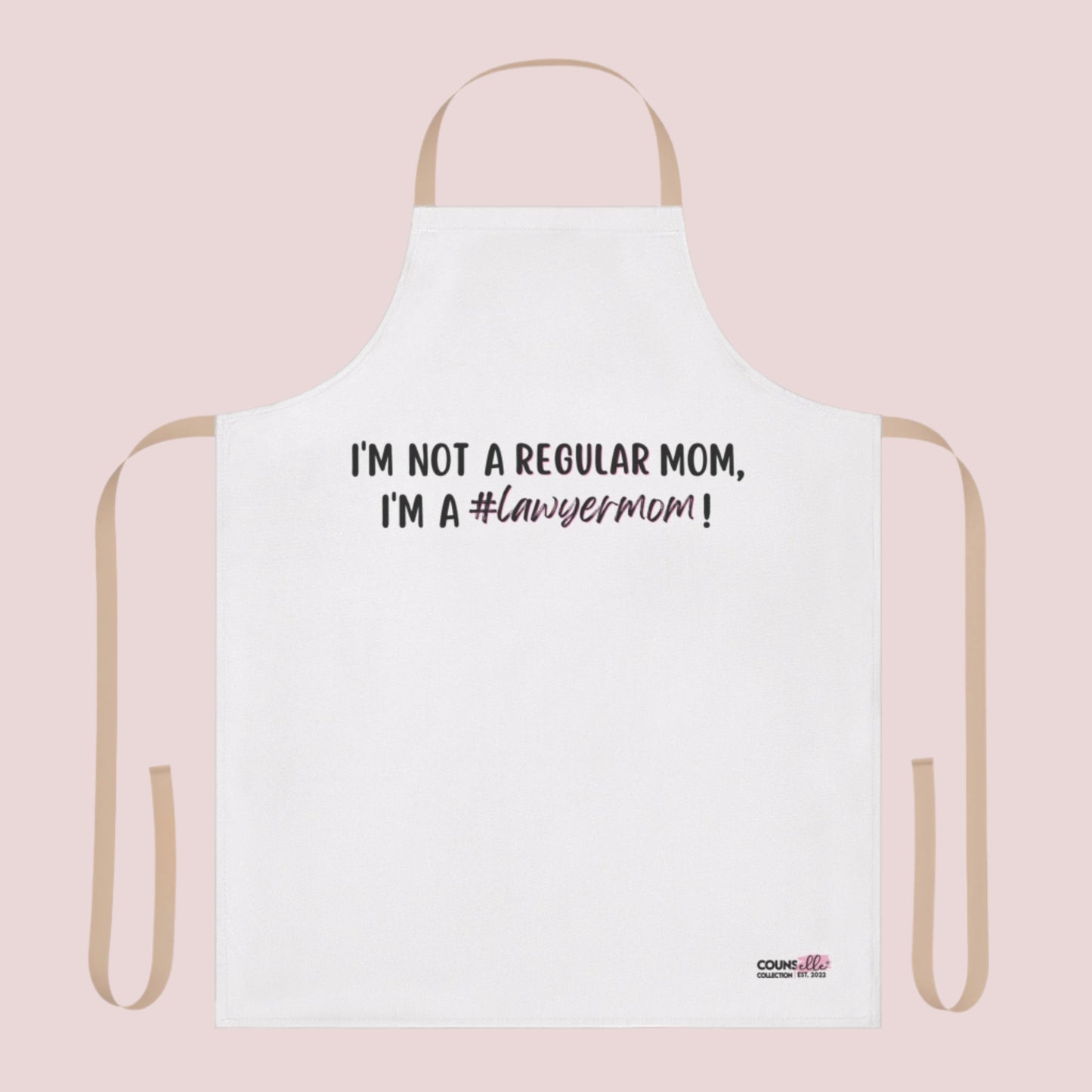 A white apron with the text "I'm not a regular mom, I'm a #lawyermom!" and the counsellecollection logo on the bottom right corner. The apron has a neutral/beige strap and belt.