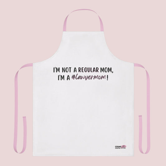 A white apron with the text "I'm not a regular mom, I'm a #lawyermom!"  and the counsellecollection logo on the bottom right corner. The apron has a pink neck strap and pink belt.