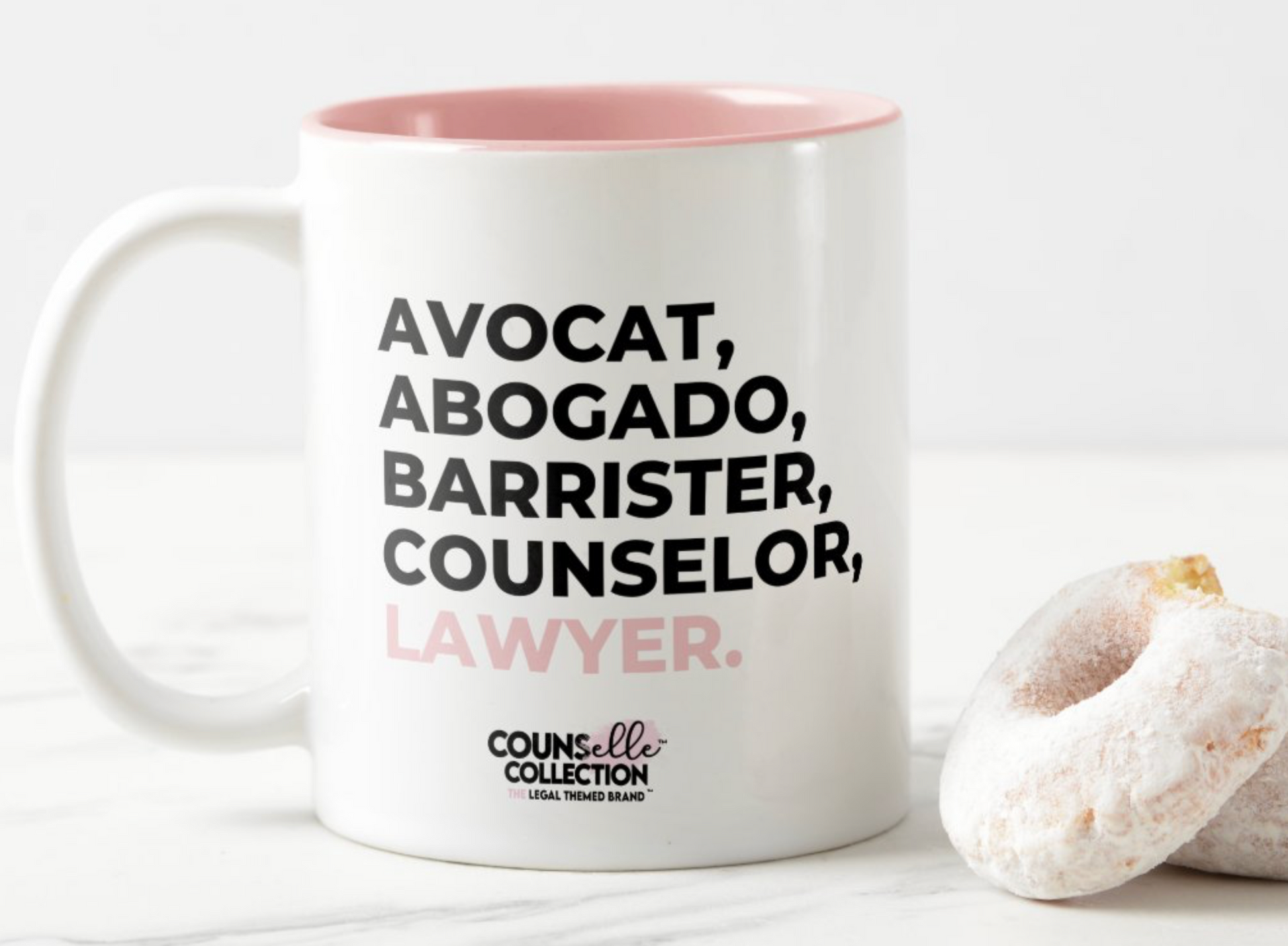 A white mug with a blush pink rim and inside color, with the text "avocat", "abogado", "barrister", "counselor", "legale", and "lawyer" on the front. Counselle Collection® logo under text.