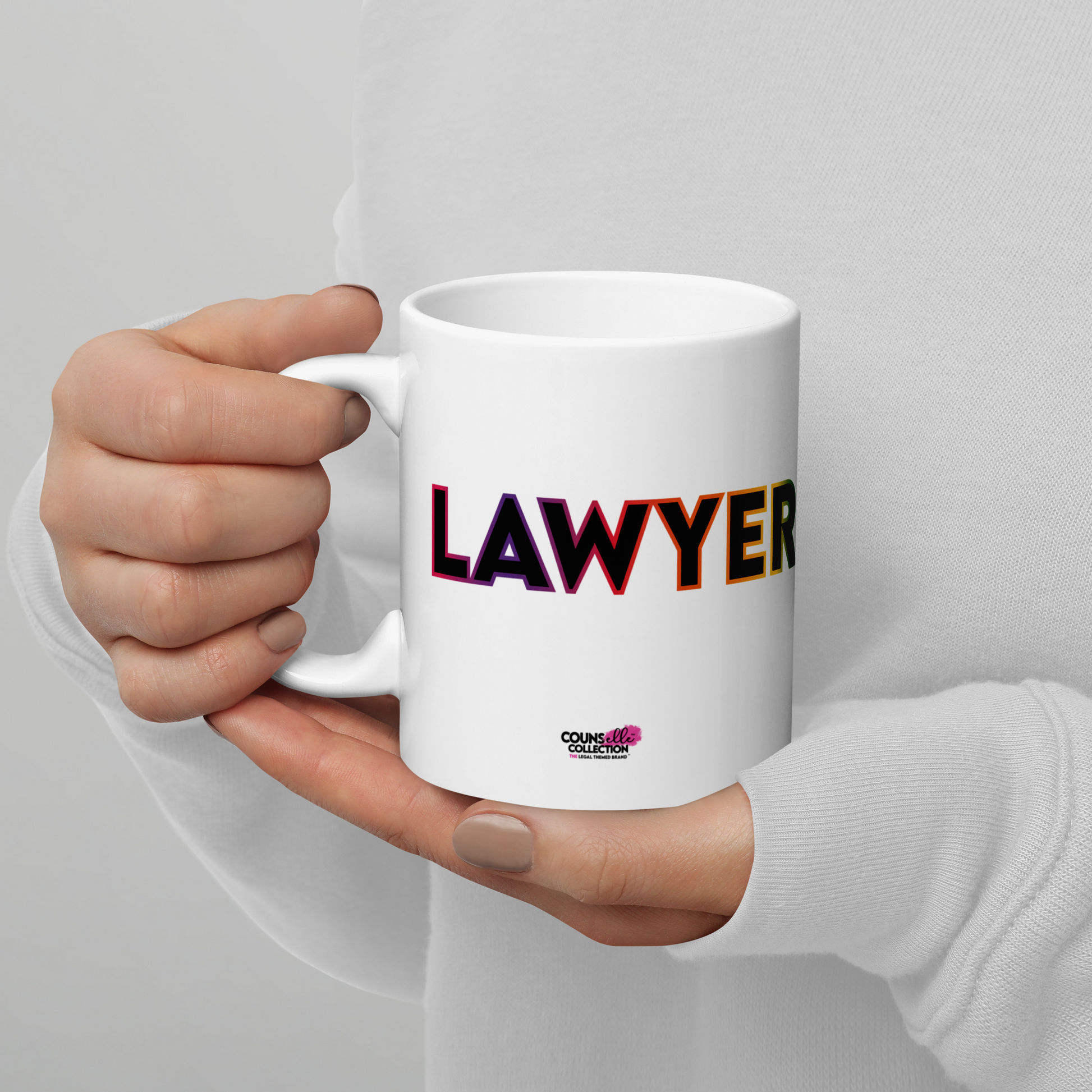A model holding a white mug showing the word "LAWYER" with a rainbow-colored outline, and the counsellecollection logo at the bottom of the design.