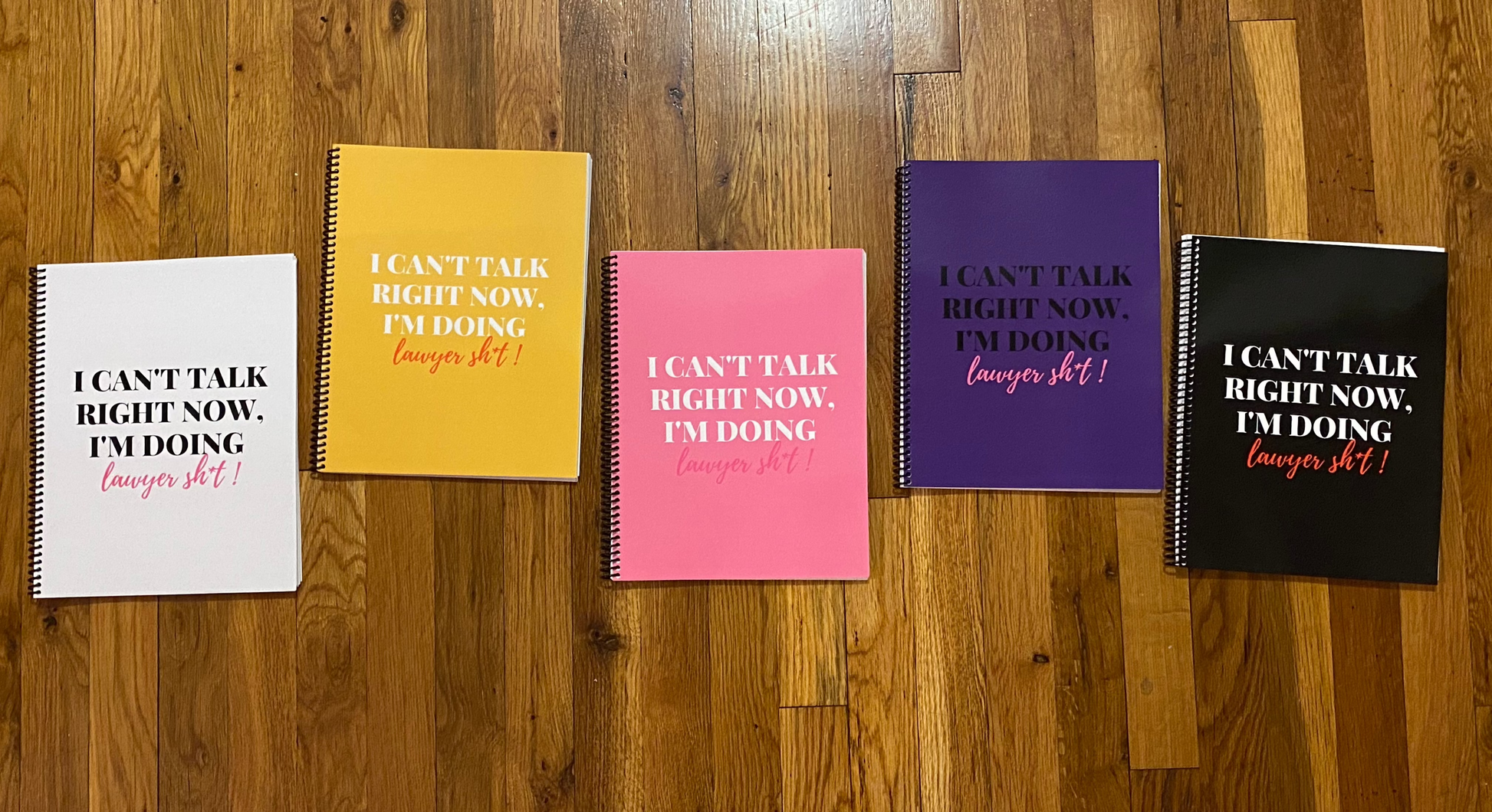5 notebooks, laying on a wood floor, with the phrase "I can’t talk right now, I’m doing Lawyer sh*t" on the front covers. Ring-bound with ruled pages.