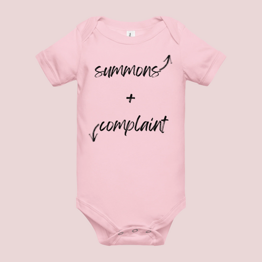 A pink infant onesie with an enveloped collar and three-snap closure, showing the text "summons" and an upward pointing arrow, and the text "complaint", and a downward pointing arrow.