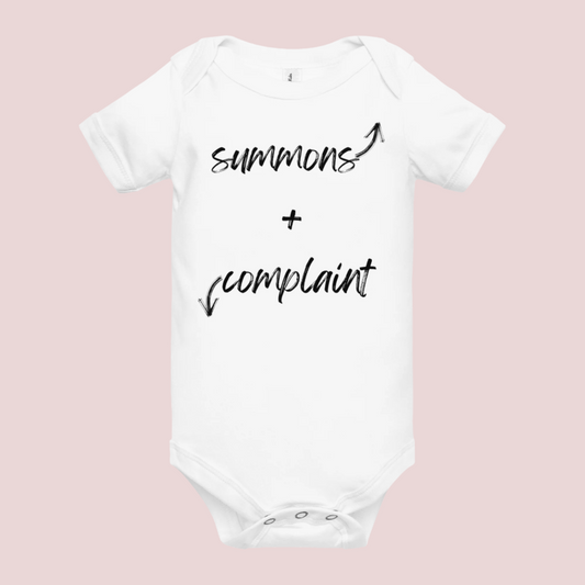 A white infant onesie with an enveloped collar and three-snap closure, showing the text "summons" and an upward pointing arrow, and the text "complaint", and a downward pointing arrow.