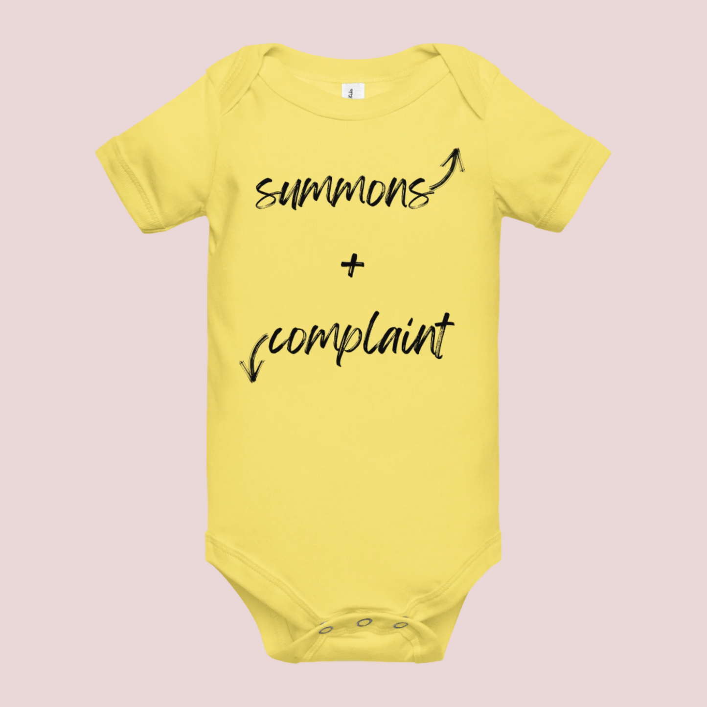 A yellow infant onesie with an enveloped collar and three-snap closure, showing the text "summons" and an upward pointing arrow, and the text "complaint", and a downward pointing arrow.