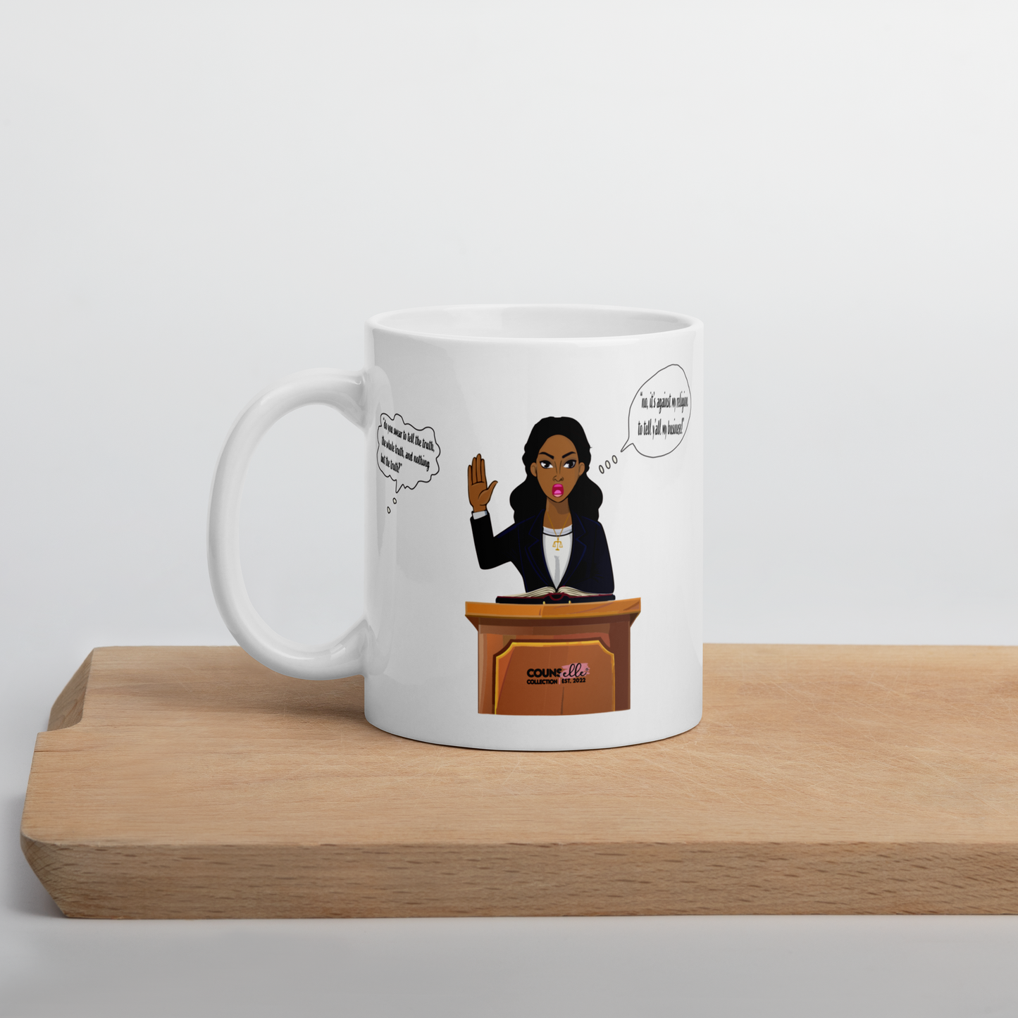 A white mug sitting on a solid wood board on a desk with an illustration of a black woman with her hand raised, testifying in court. Speech bubble that says "It's against my religion to tell yall my business".