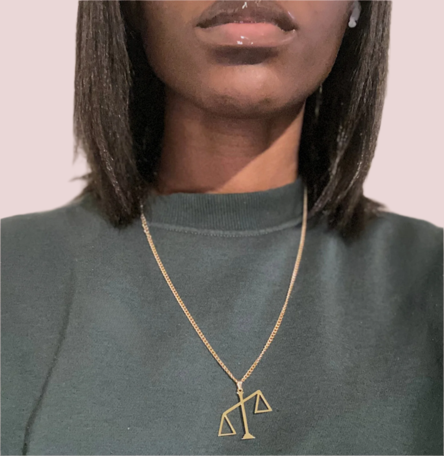 A gold chain necklace featuring a pendant in the shape of the scales of justice tipped to one side.