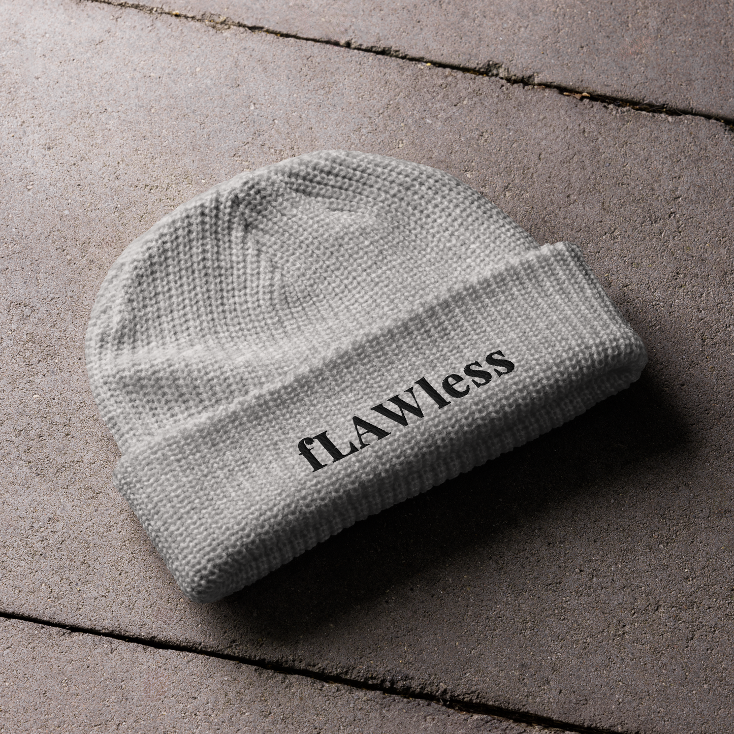 A grey beanie with the text "fLAWless" in black text written on it.