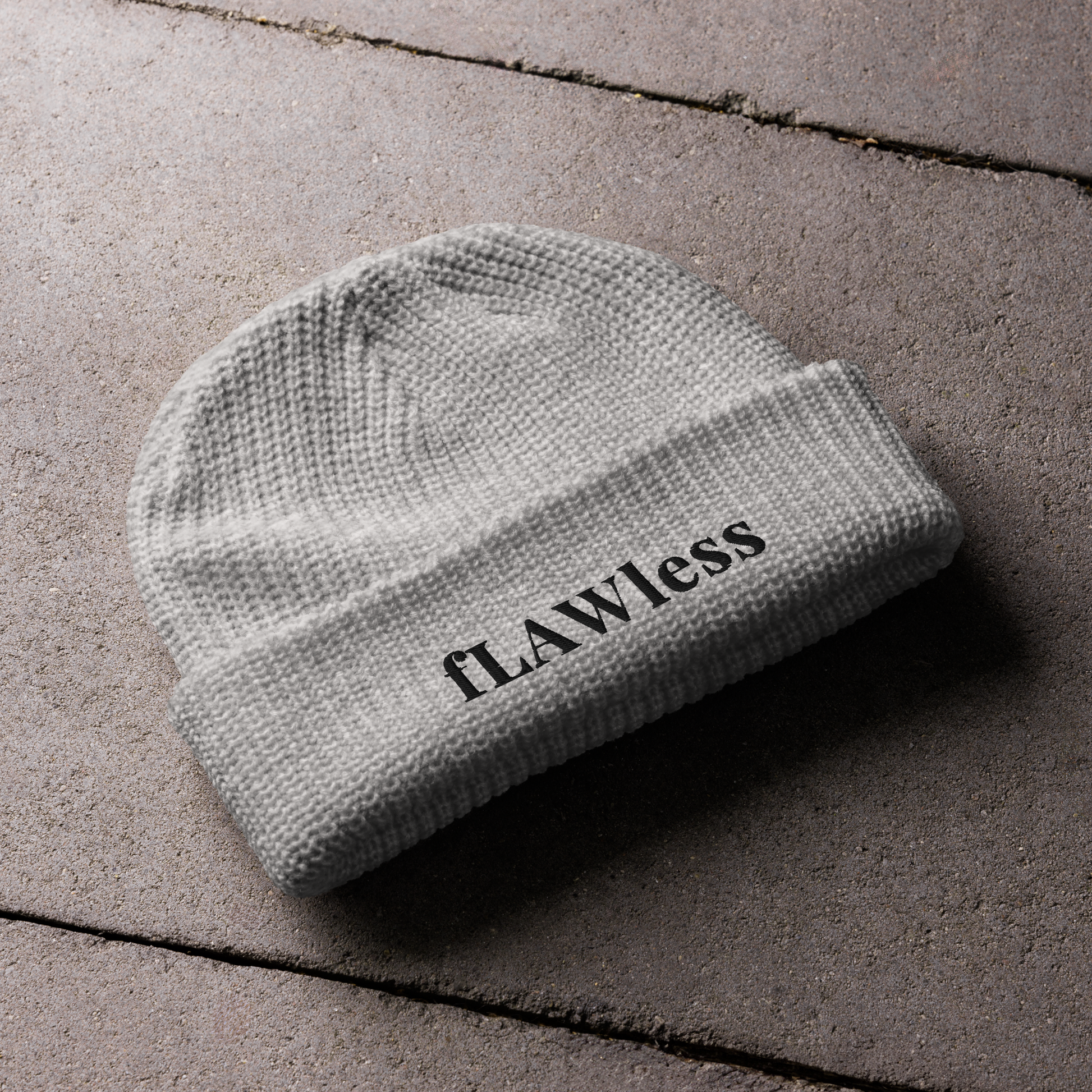 A grey beanie with the text "fLAWless" in black text written on it.
