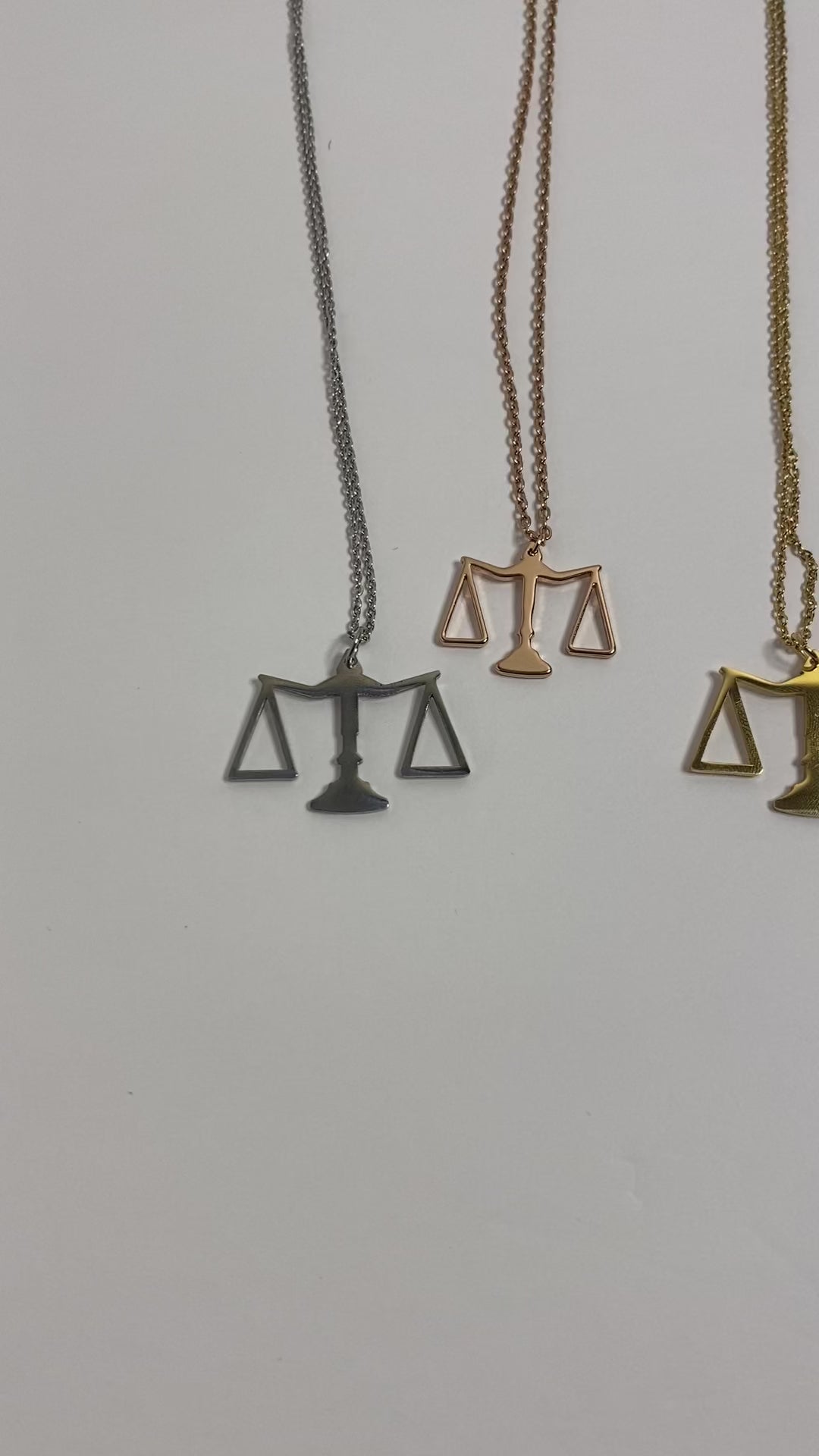 A stainless steel piece with 18k gold plating, featuring a sleek pendant in the shape of the scales of justice. Available in gold, rose gold, and silver.