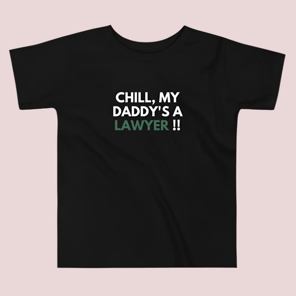A black roundneck kid's tee featuring the quote "Chill my daddy's a lawyer" in uppercase text.