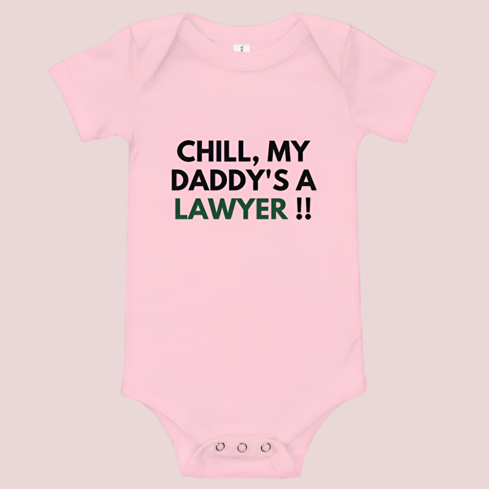A pink baby onesie with a three-snap leg closure featuring the quote "Chill my daddy's a lawyer" in uppercase block text.