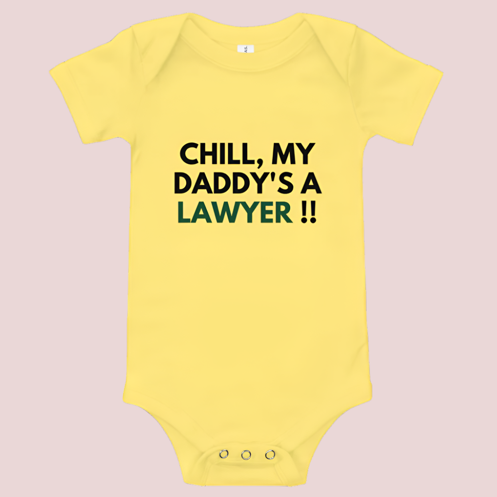 A yellow baby onesie with a three-snap leg closure featuring the quote "Chill my daddy's a lawyer" in uppercase block text.