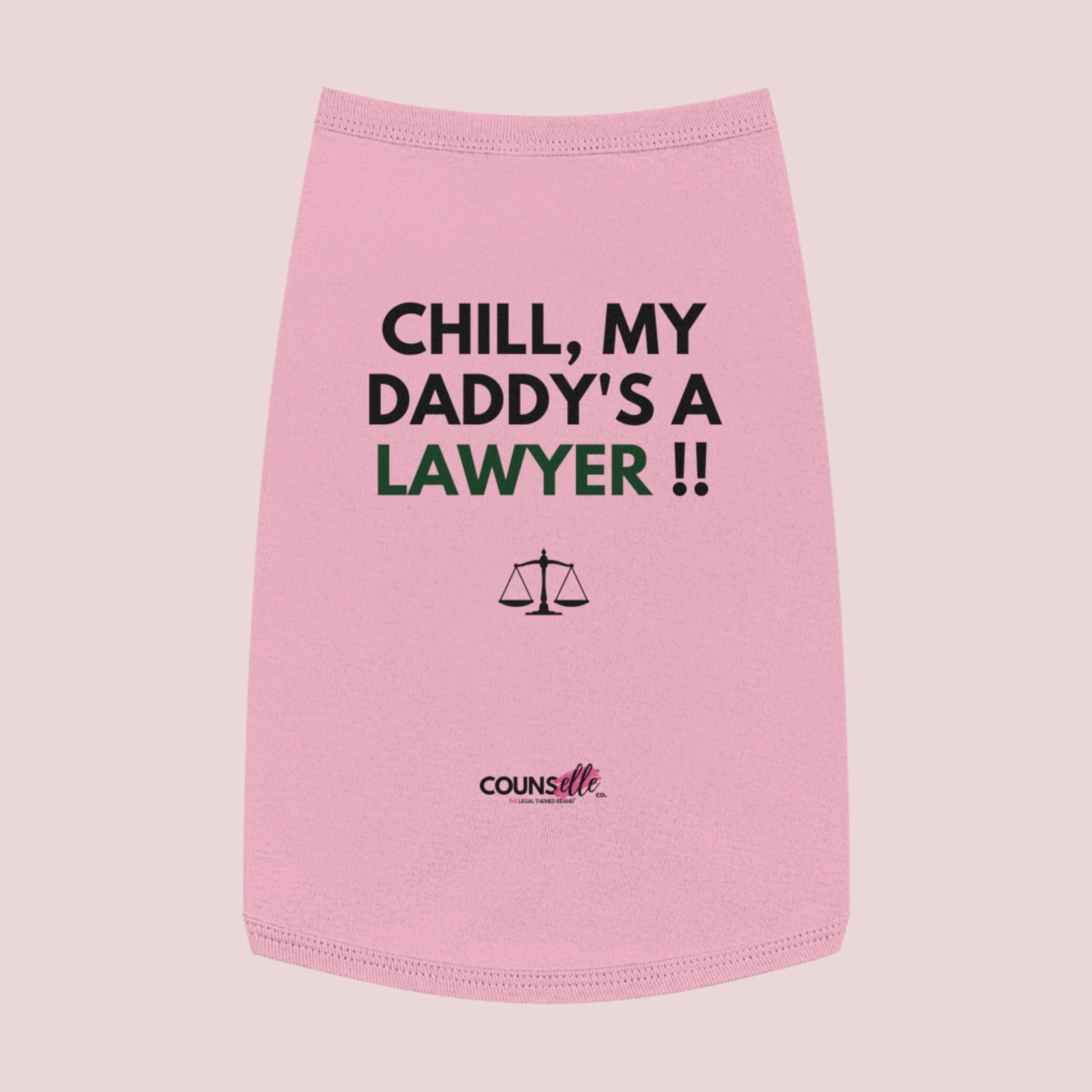 A pink pet tee featuring the quote "Chill, my daddy's a lawyer" in uppercase text, an illustration of justice scales below the text and the counsellecollection logo near the hem.