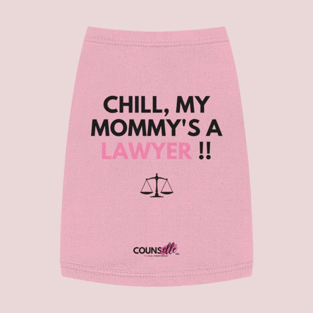 A pink pet tee featuring the quote "Chill, my mommy's a lawyer" in uppercase text, an illustration of justice scales below the text and the counsellecollection logo near the hem..