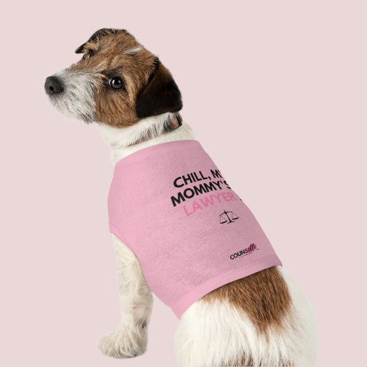 A dog wearing A pink pet tee featuring the quote "Chill, my mommy's a lawyer" in uppercase text, an illustration of justice scales below the text and the counsellecollection logo near the hem.