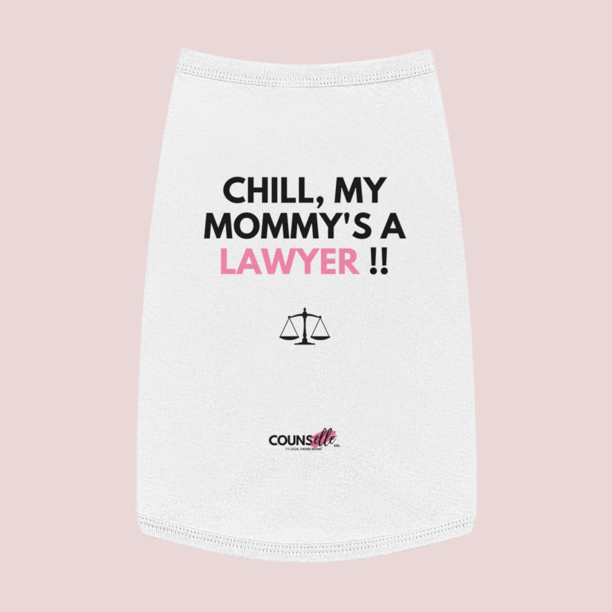 A white pet tee featuring the quote "Chill, my mommy's a lawyer" in uppercase text, an illustration of justice scales below the text and the counsellecollection logo near the hem.