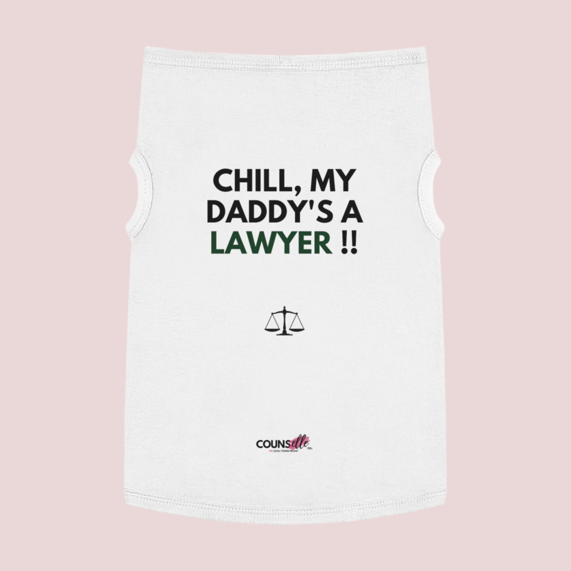 A white pet tee featuring the quote "Chill, my daddy's a lawyer" in uppercase text, an illustration of justice scales below the text and the counsellecollection logo near the hem.