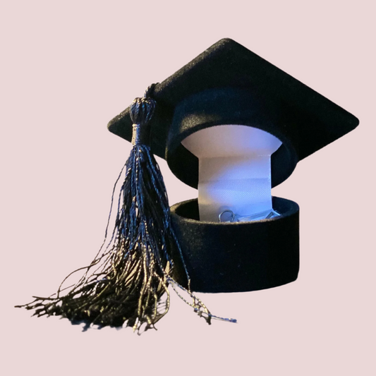 A fabric-lined, black jewelry box in the shape of a graduation cap with a black tassel on the side.