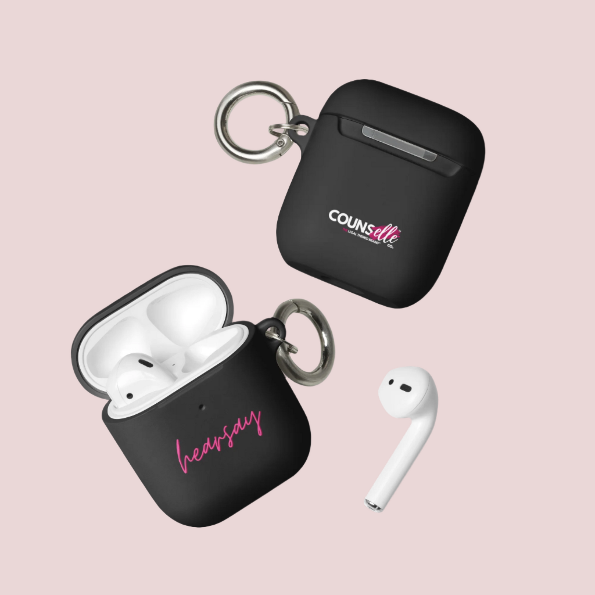 Two black AirPods Cases showing the word "hearsay" in script font on one of the cases and the counsellecollection logo on the other. A single airpod can also be seen beside one of the cases.