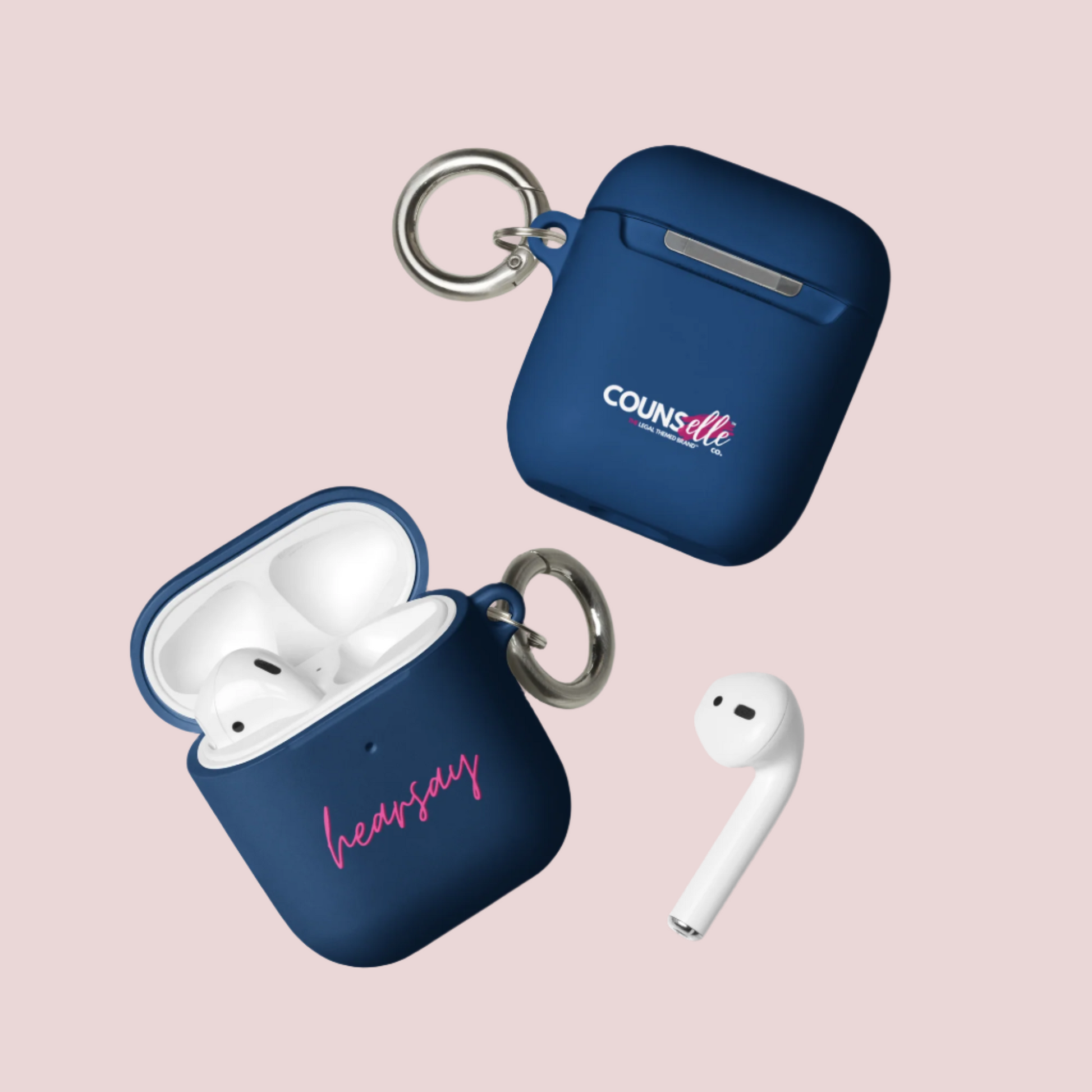 Two navy blue AirPods Cases showing the word "hearsay" in script font on one of the cases and the counsellecollection logo on the other. A single airpod can also be seen beside one of the cases.