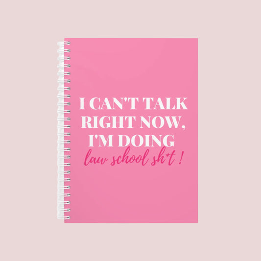 A pink wire bound notebook with the text "I can't talk right now, I'm doing law school sh*t" on the cover.