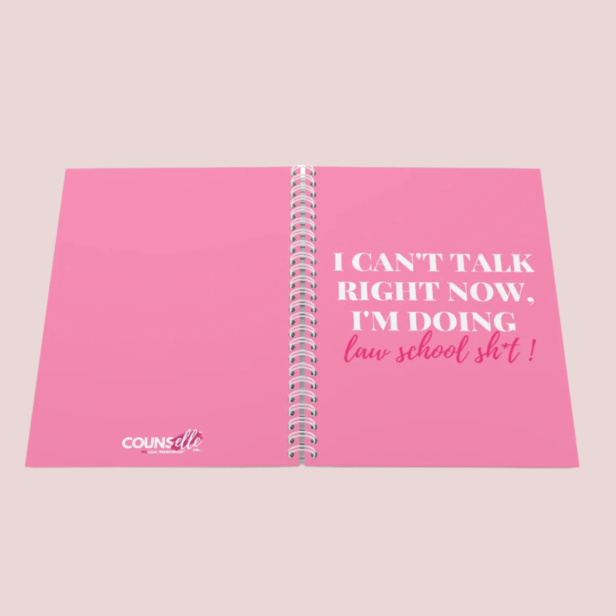A pink wire bound notebook with the text "I can't talk right now, I'm doing law school sh*t" on the cover and the counsellecollection logo at the bottom center part of the back cover.
