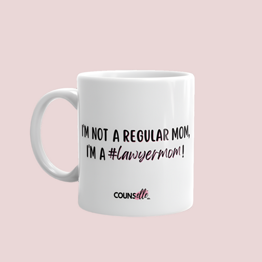 A white mug showing the text "I AM NOT A REGULAR MOM, I'M A #LawyerMom" with the counsellecollection logo at the bottom of the design.