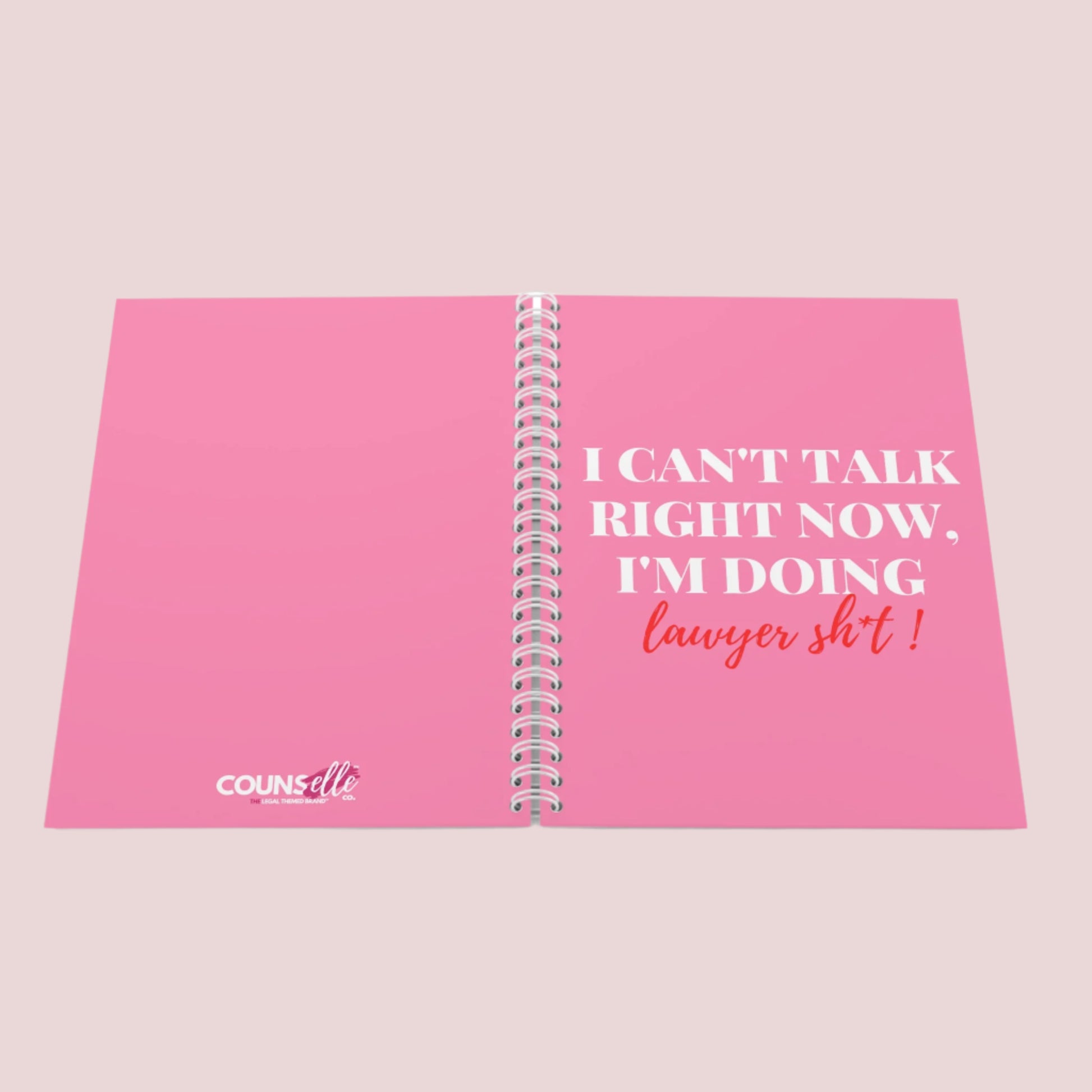 A pink notebook with the phrase "I can’t talk right now, I’m doing Lawyer sh*t" on the front cover and counselle collection logo on the back cover. Ring-bound with ruled pages.